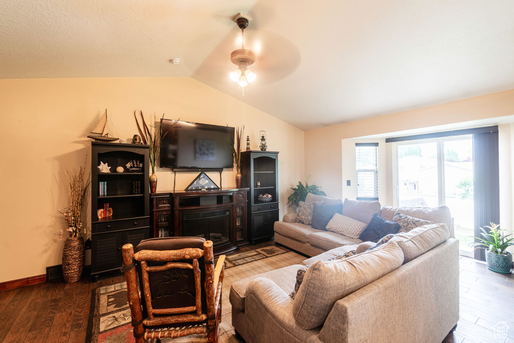 Living room featuring wood-type flooring, ceiling fan, a fireplace, and vaulted ceiling