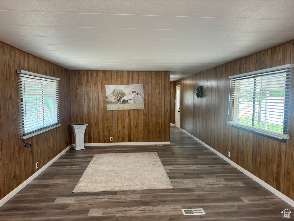 Empty room featuring a textured ceiling, wood walls, and dark hardwood / wood-style flooring