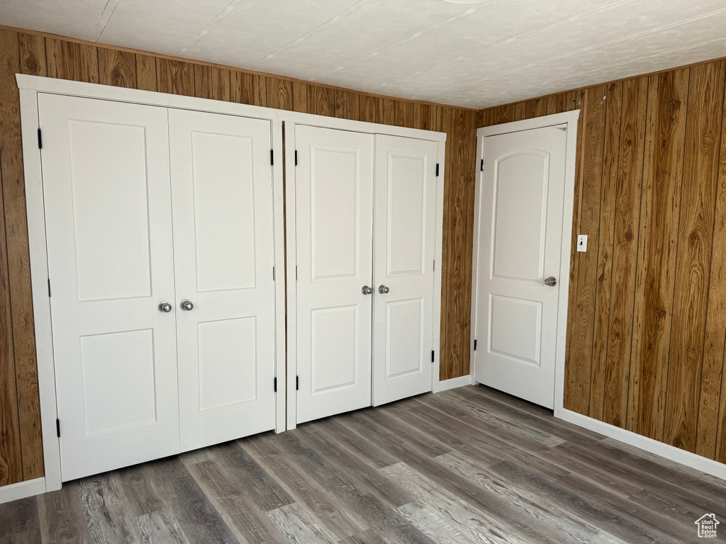 Unfurnished bedroom with multiple closets, dark wood-type flooring, and wooden walls