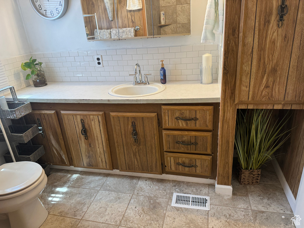 Bathroom featuring toilet, tile flooring, vanity, and tasteful backsplash