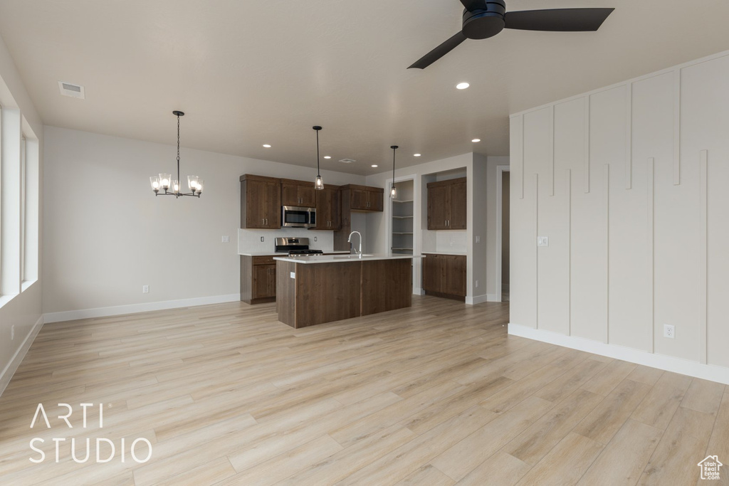 Kitchen with light hardwood / wood-style floors, hanging light fixtures, a center island with sink, and ceiling fan with notable chandelier