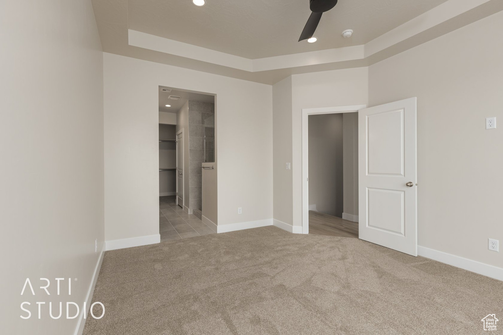 Unfurnished bedroom featuring ensuite bath, ceiling fan, a tray ceiling, and light carpet