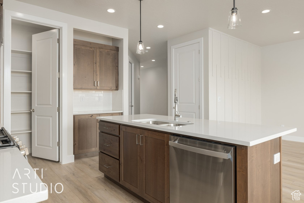 Kitchen featuring light wood-type flooring, a kitchen island with sink, decorative light fixtures, tasteful backsplash, and dishwasher