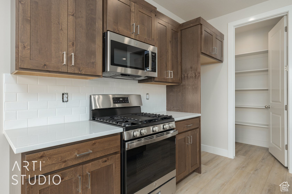 Kitchen with stainless steel appliances, dark brown cabinetry, backsplash, and light wood-type flooring