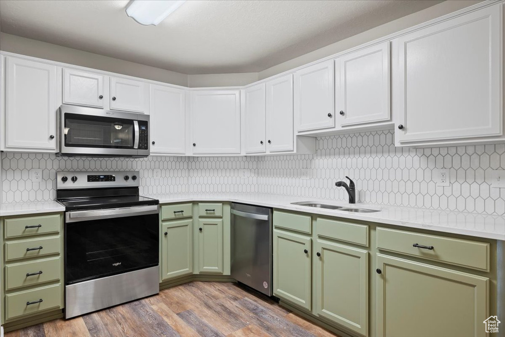 Kitchen with hardwood / wood-style floors, backsplash, green cabinets, white cabinets, and appliances with stainless steel finishes