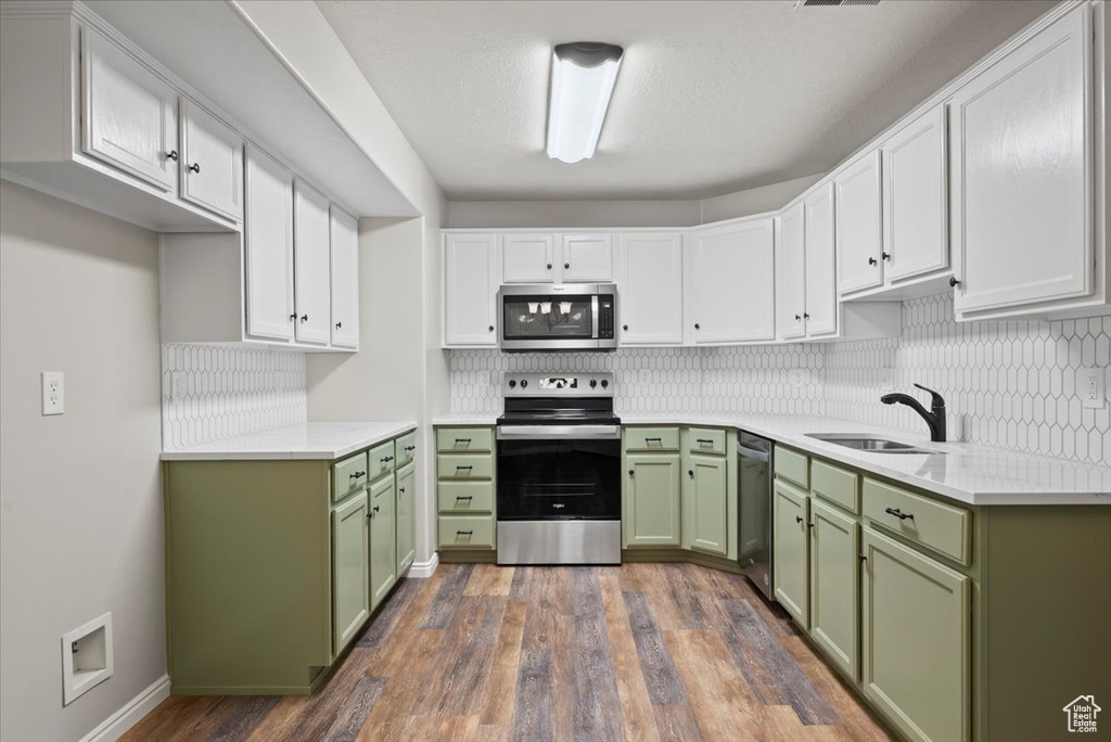 Kitchen with stainless steel appliances, dark wood-type flooring, sink, green cabinets, and white cabinetry