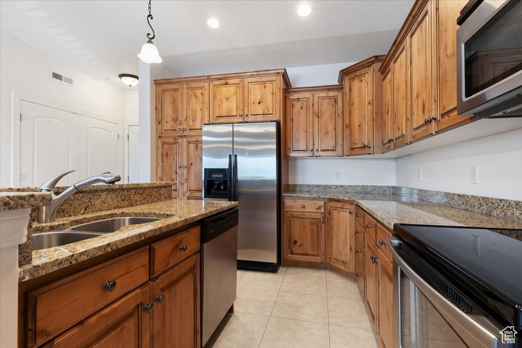 Kitchen with appliances with stainless steel finishes, light stone counters, pendant lighting, sink, and light tile floors