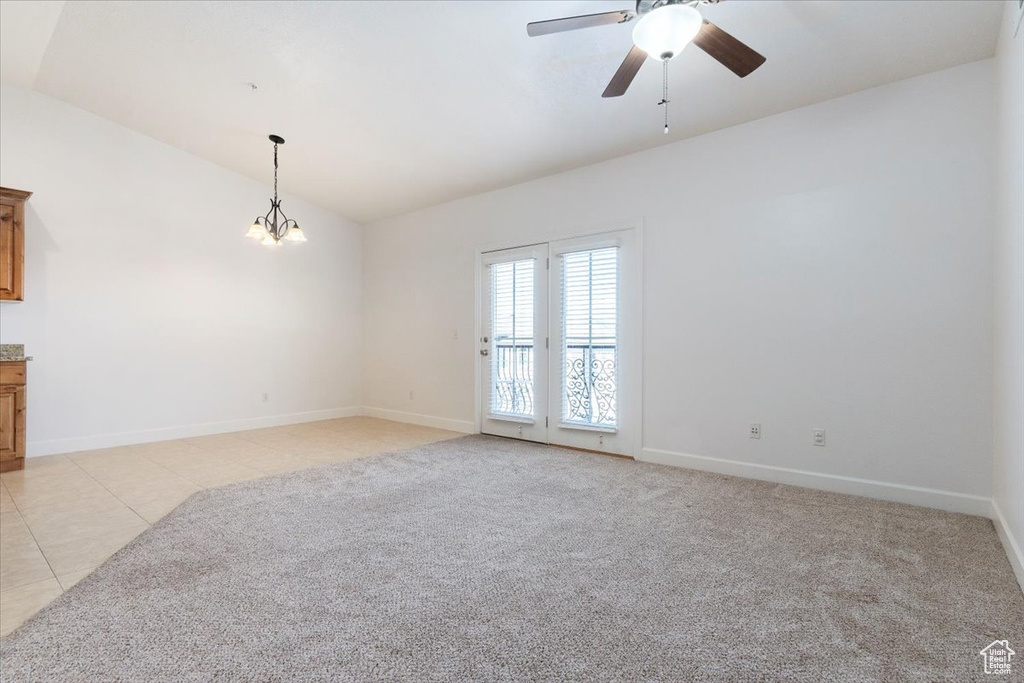 Carpeted spare room featuring lofted ceiling and ceiling fan with notable chandelier