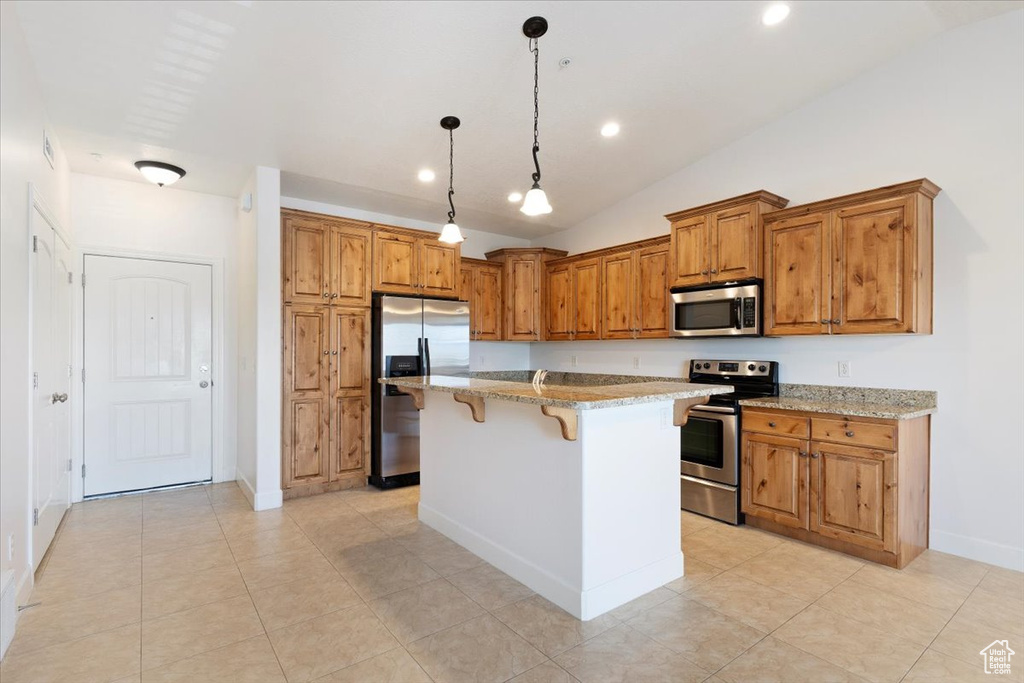 Kitchen with a center island, a kitchen breakfast bar, stainless steel appliances, light stone counters, and decorative light fixtures