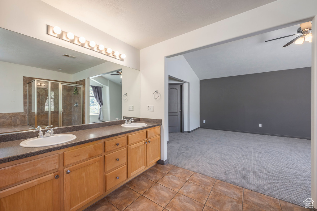 Bathroom with vaulted ceiling, vanity with extensive cabinet space, dual sinks, ceiling fan, and tile flooring