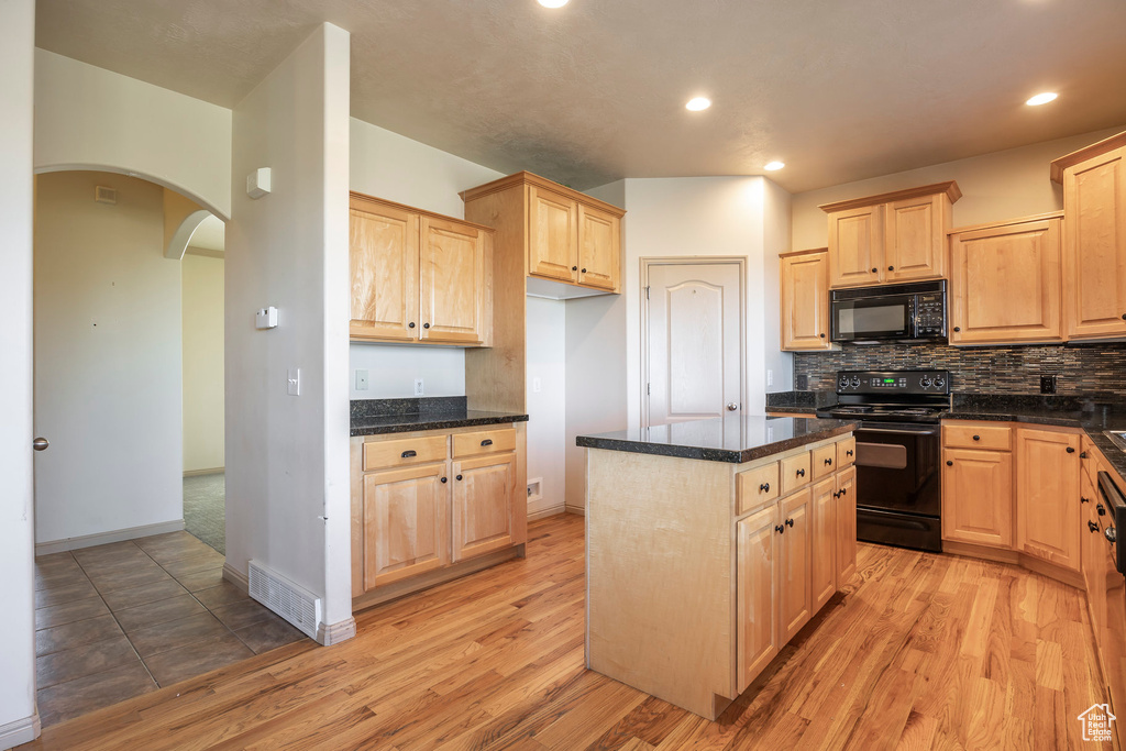 Kitchen featuring light brown cabinets, light tile floors, black appliances, and a center island