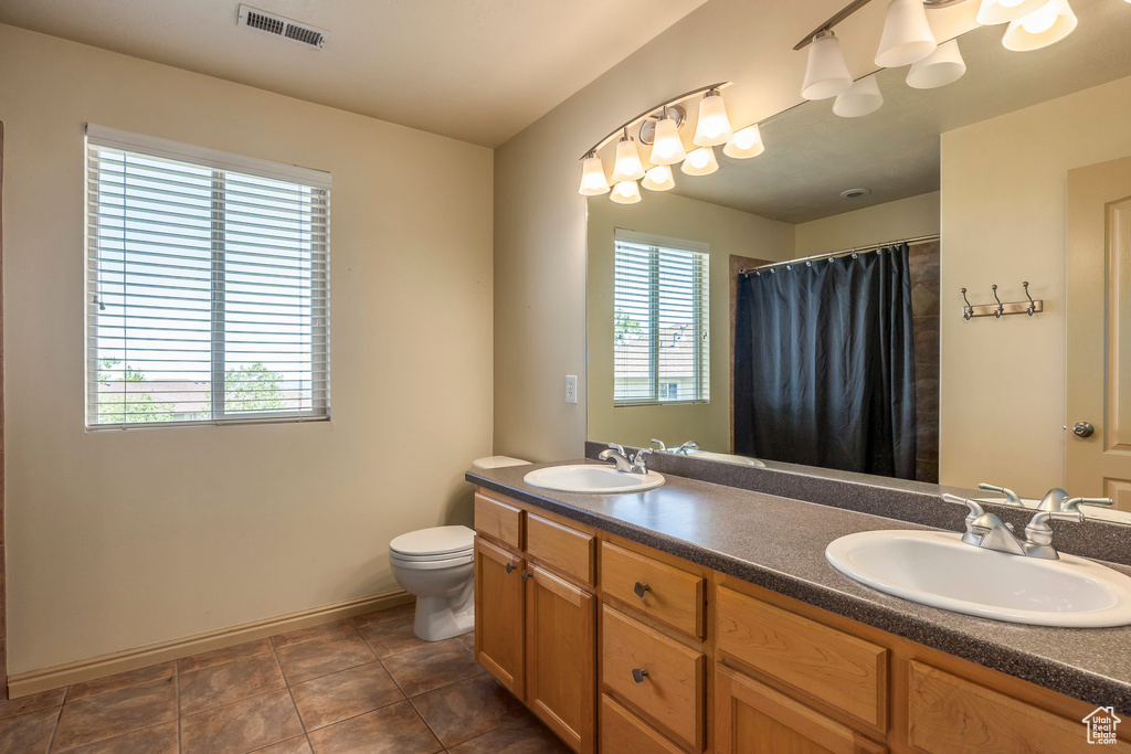 Bathroom with a wealth of natural light, double vanity, toilet, and tile floors