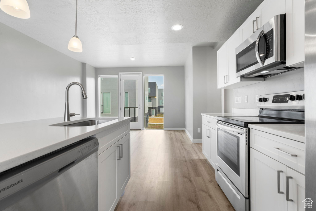 Kitchen featuring stainless steel appliances, hanging light fixtures, light wood-type flooring, white cabinets, and sink