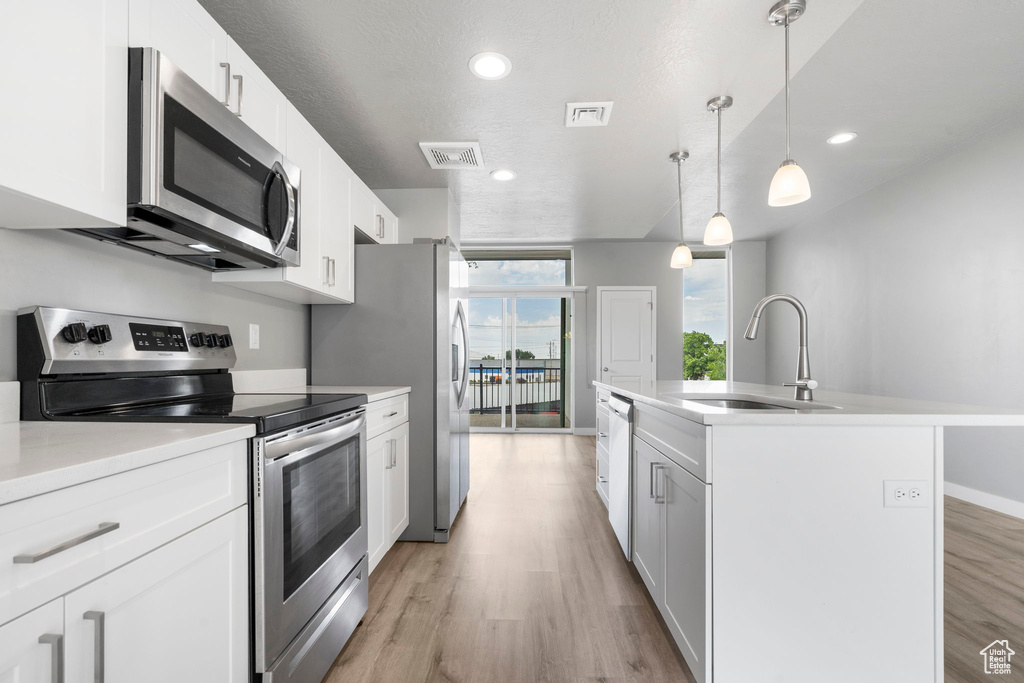 Kitchen featuring appliances with stainless steel finishes, a kitchen island with sink, pendant lighting, and light hardwood / wood-style flooring