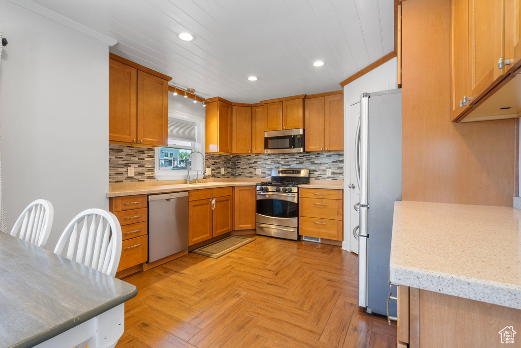 Kitchen with light stone countertops, appliances with stainless steel finishes, backsplash, light parquet flooring, and sink