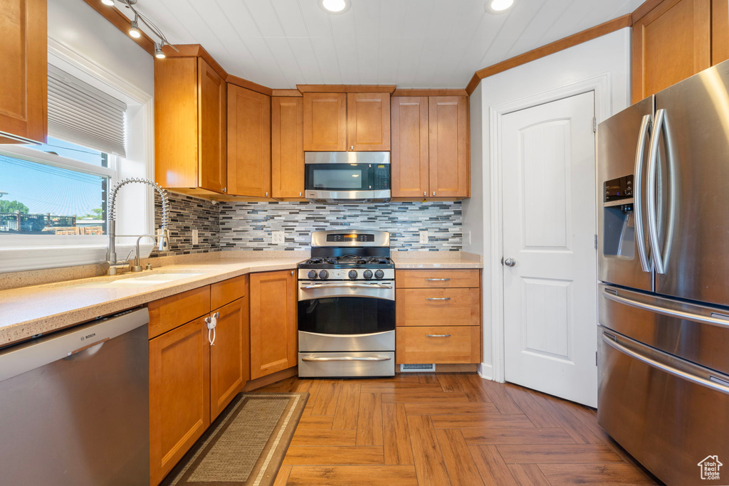 Kitchen featuring ornamental molding, appliances with stainless steel finishes, backsplash, light parquet floors, and track lighting