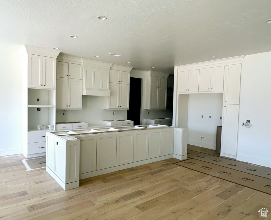 Kitchen featuring a textured ceiling, a kitchen island, light hardwood / wood-style floors, white cabinetry, and custom exhaust hood