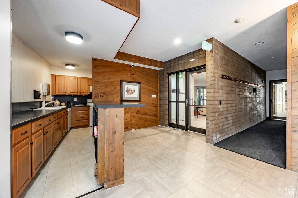 Kitchen with a textured ceiling, wooden walls, a breakfast bar, sink, and light tile flooring