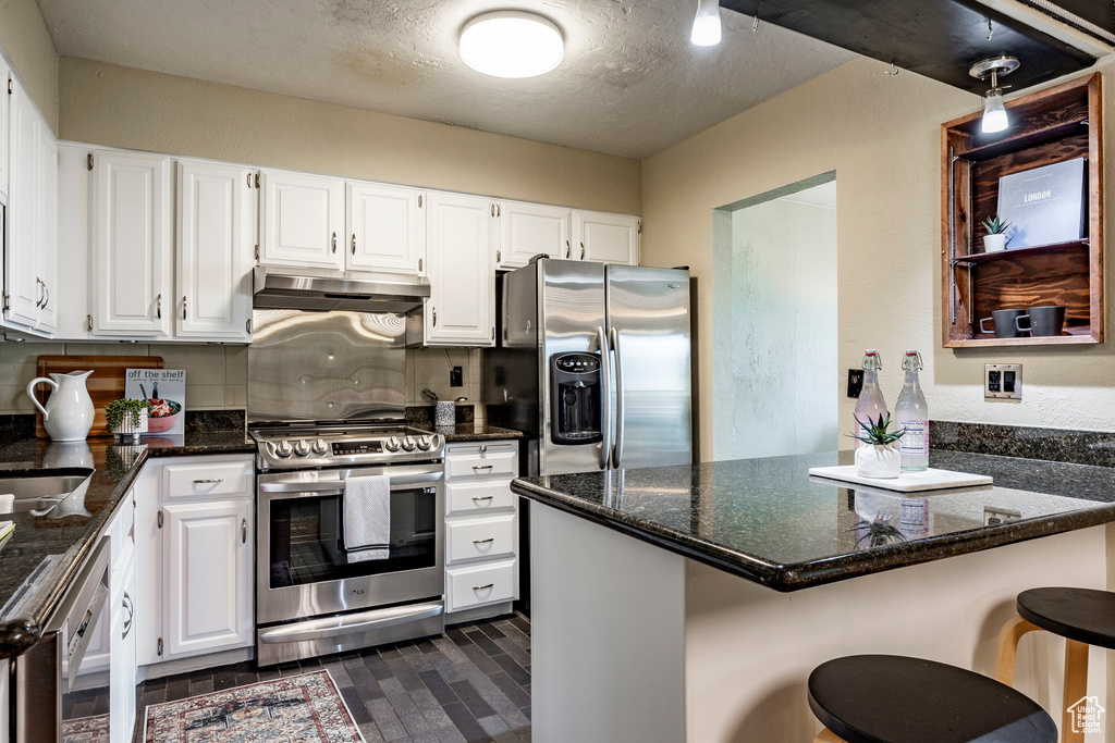 Kitchen with kitchen peninsula, stainless steel appliances, dark stone countertops, white cabinets, and a kitchen bar