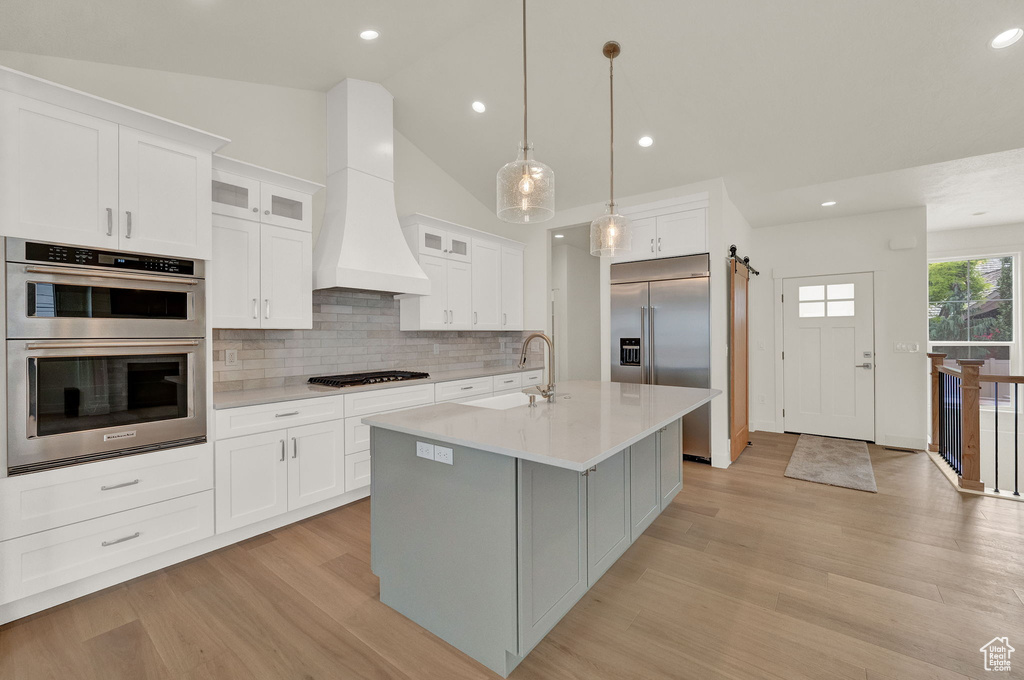 Kitchen with custom range hood, light hardwood / wood-style floors, tasteful backsplash, white cabinetry, and appliances with stainless steel finishes