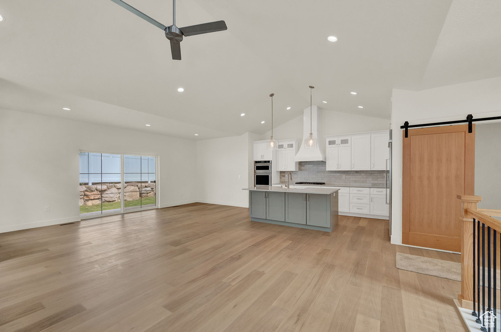 Kitchen featuring light hardwood / wood-style floors, a center island with sink, tasteful backsplash, white cabinetry, and pendant lighting