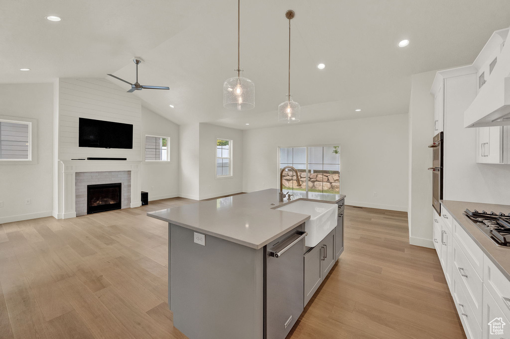 Kitchen featuring light hardwood / wood-style floors, stainless steel appliances, a fireplace, sink, and lofted ceiling