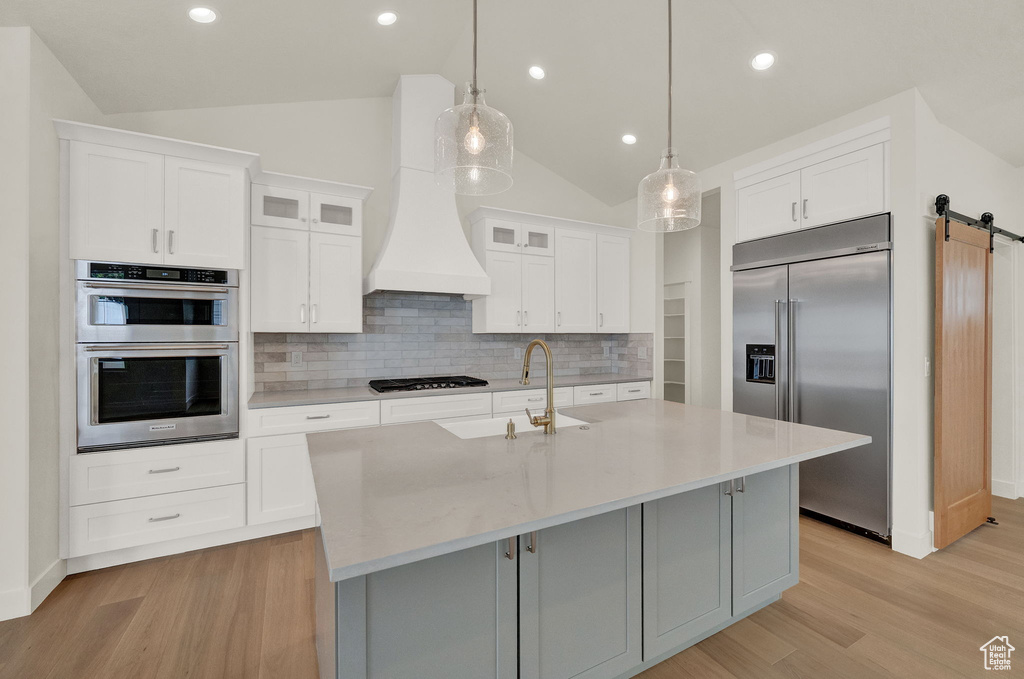 Kitchen with white cabinetry, stainless steel appliances, a barn door, tasteful backsplash, and vaulted ceiling