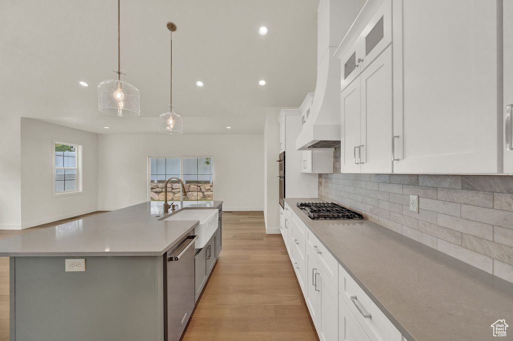 Kitchen with decorative light fixtures, light hardwood / wood-style flooring, tasteful backsplash, white cabinetry, and an island with sink