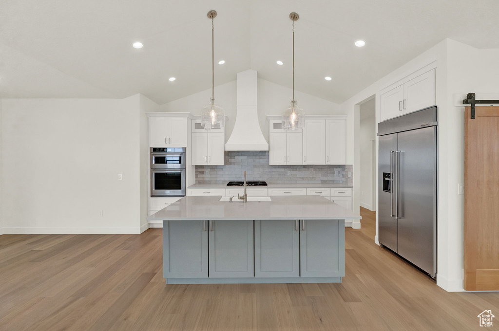 Kitchen featuring stainless steel appliances, light hardwood / wood-style floors, premium range hood, and lofted ceiling