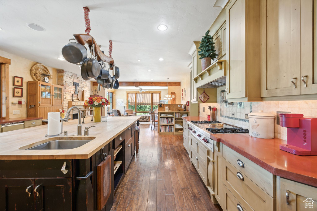 Kitchen with dark wood-type flooring, wood counters, a center island with sink, sink, and tasteful backsplash