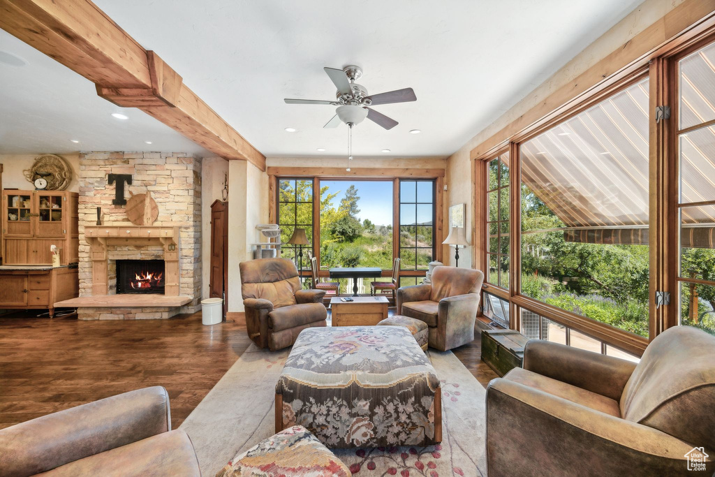 Living room with a stone fireplace, hardwood / wood-style flooring, ceiling fan, and beamed ceiling