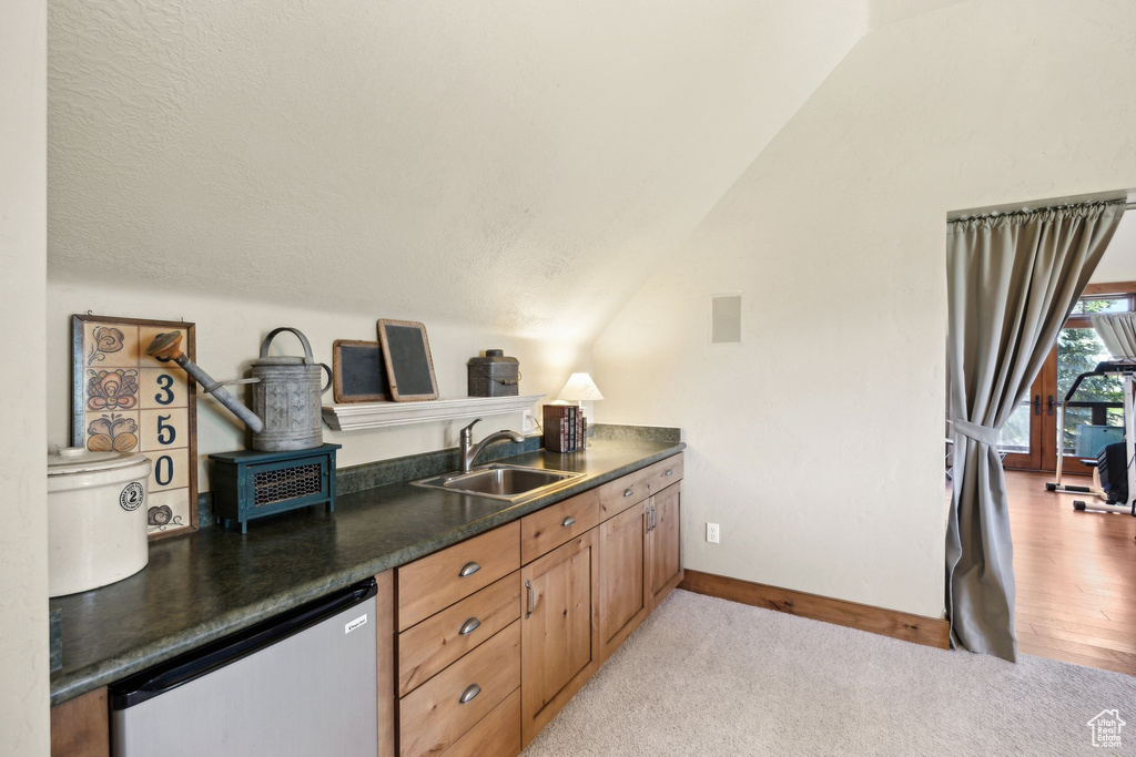 Kitchen featuring sink, dishwasher, vaulted ceiling, and light colored carpet