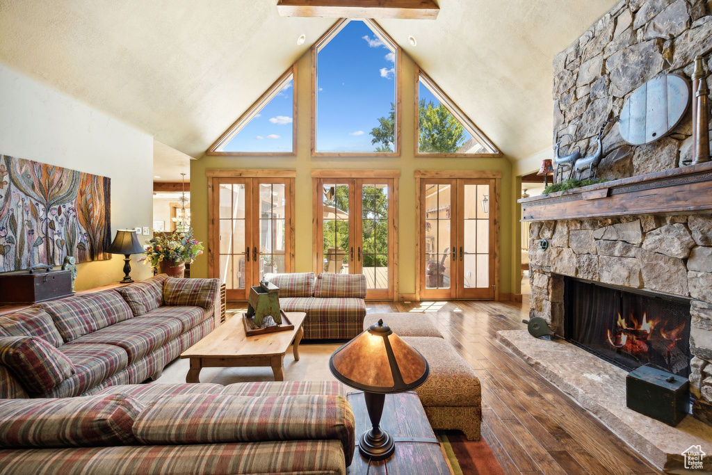 Living room featuring a stone fireplace, high vaulted ceiling, french doors, and hardwood / wood-style floors