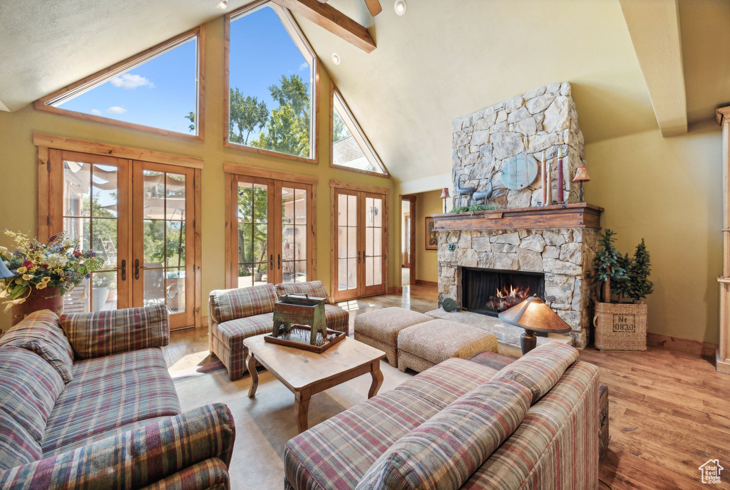 Living room featuring a stone fireplace, french doors, hardwood / wood-style floors, beamed ceiling, and high vaulted ceiling