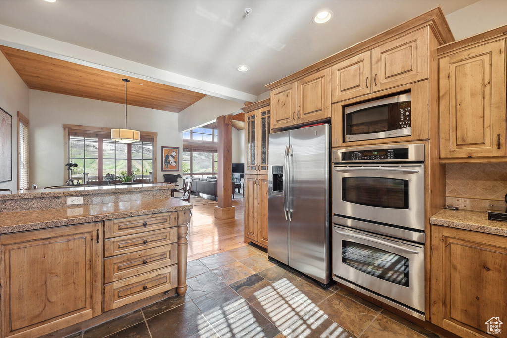 Kitchen with dark tile floors, hanging light fixtures, tasteful backsplash, beam ceiling, and appliances with stainless steel finishes