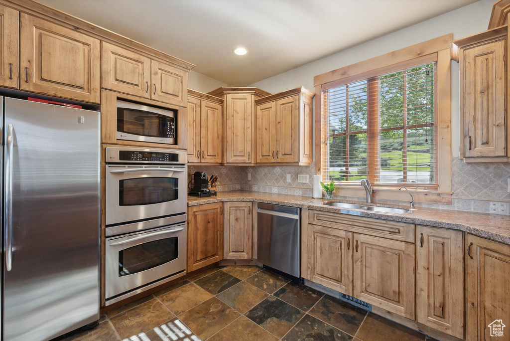 Kitchen featuring dark tile flooring, sink, tasteful backsplash, and appliances with stainless steel finishes