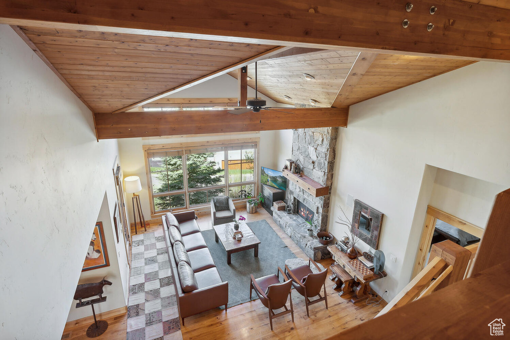 Living room featuring wood-type flooring, a stone fireplace, ceiling fan, and wood ceiling