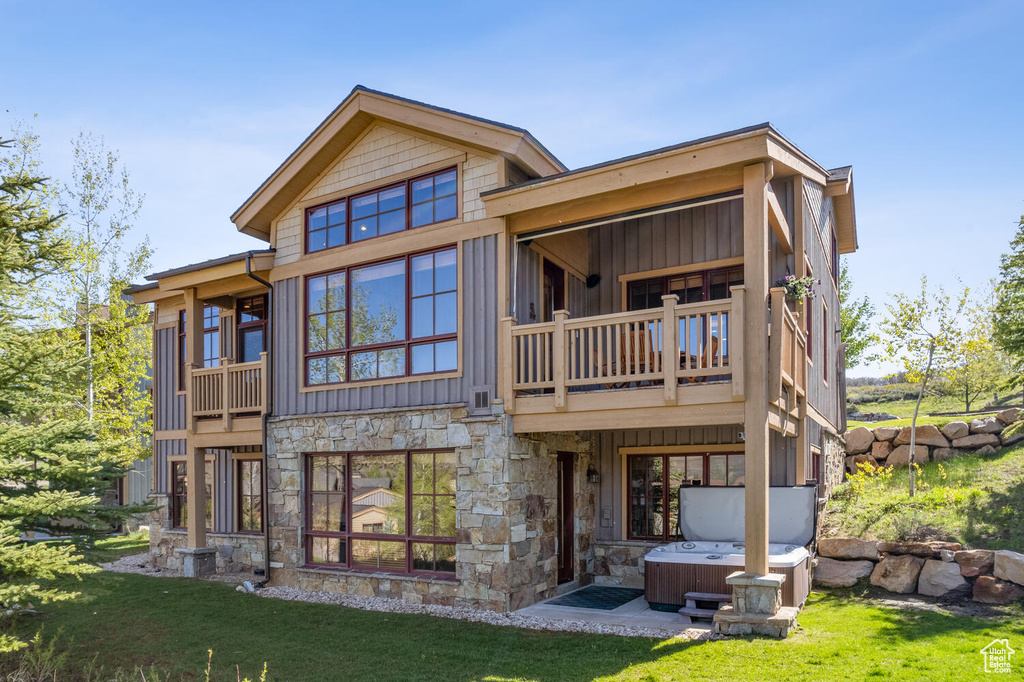 Rear view of property featuring a hot tub, a lawn, and a balcony