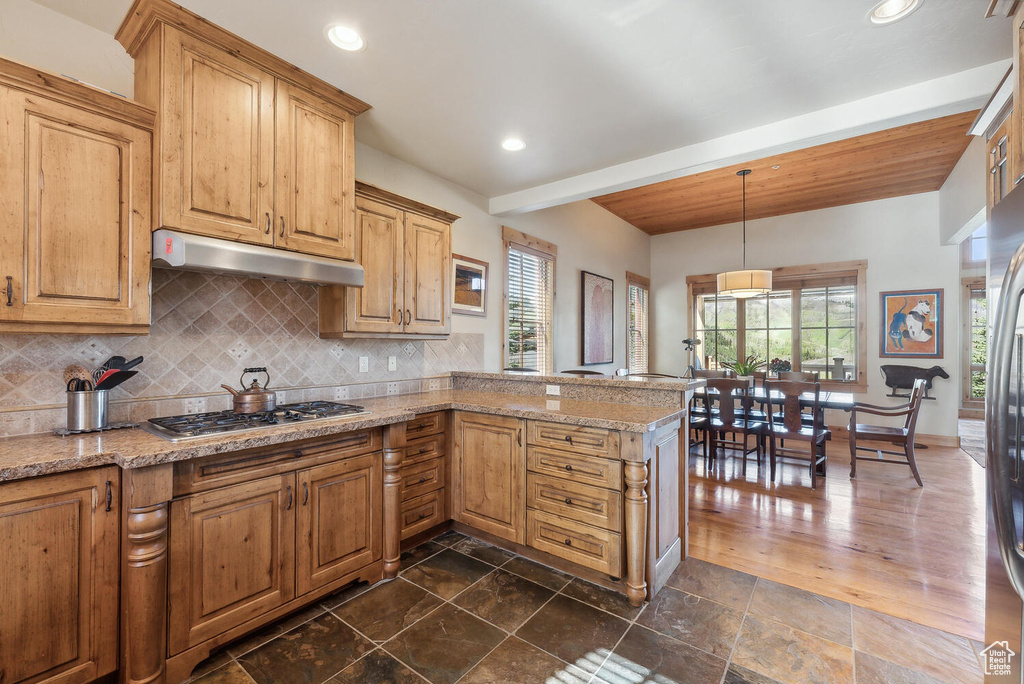 Kitchen featuring dark tile flooring, kitchen peninsula, tasteful backsplash, and appliances with stainless steel finishes