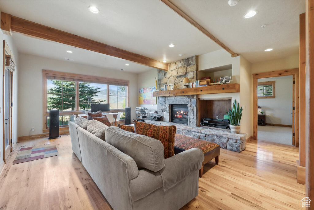 Living room with a stone fireplace, beam ceiling, and light wood-type flooring