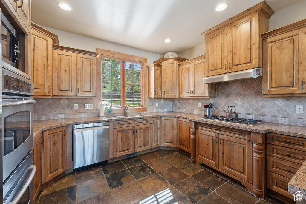 Kitchen with appliances with stainless steel finishes, light stone counters, sink, tasteful backsplash, and dark tile flooring