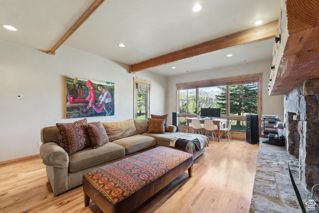 Living room with beam ceiling, a stone fireplace, and light hardwood / wood-style flooring