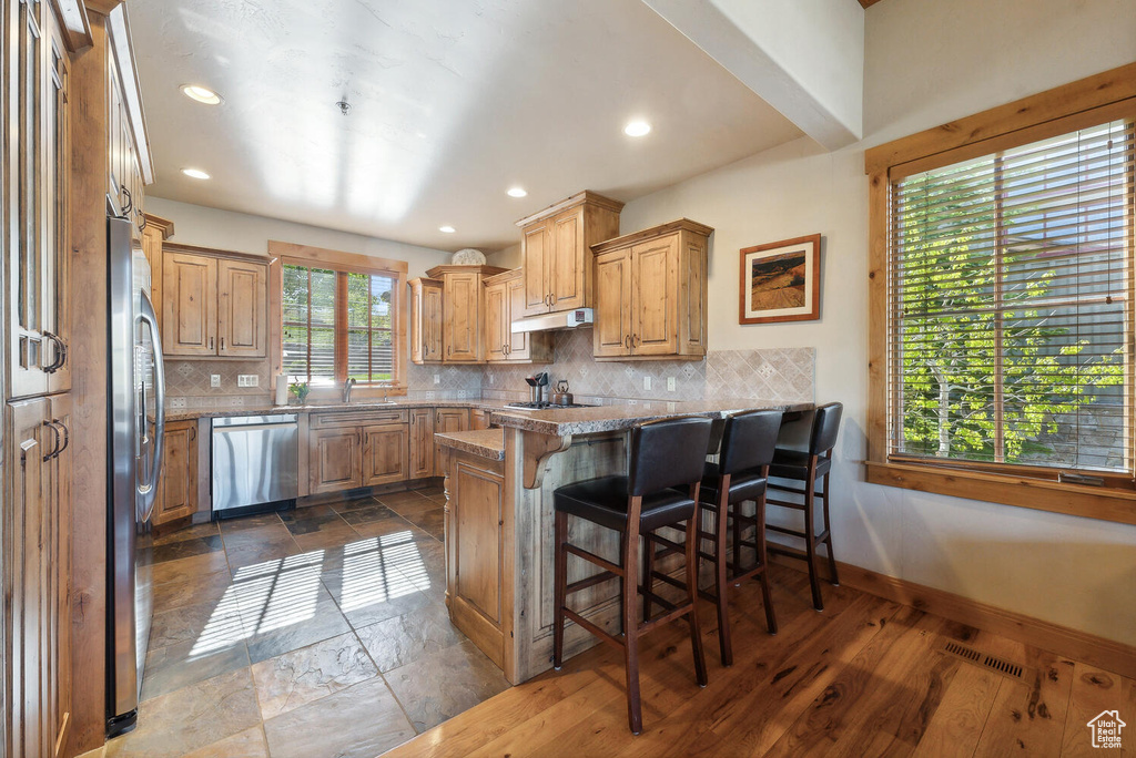 Kitchen featuring dark hardwood / wood-style flooring, kitchen peninsula, backsplash, and appliances with stainless steel finishes