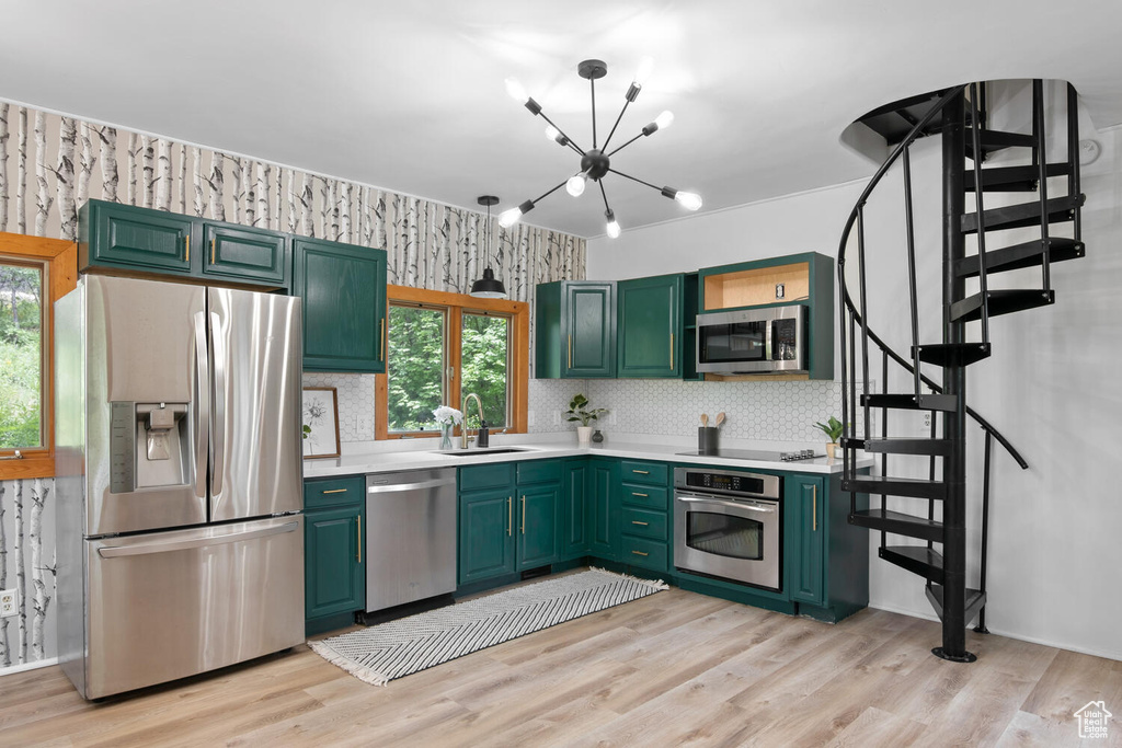 Kitchen with light hardwood / wood-style floors, stainless steel appliances, a notable chandelier, backsplash, and sink