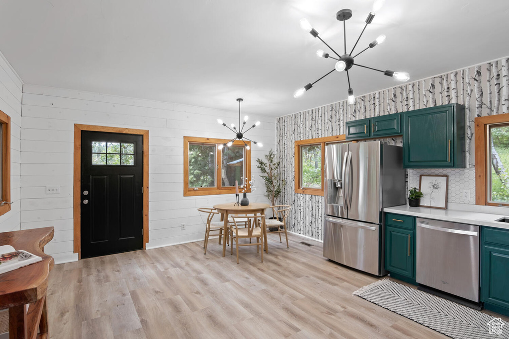 Kitchen with decorative light fixtures, an inviting chandelier, stainless steel appliances, wood walls, and light wood-type flooring