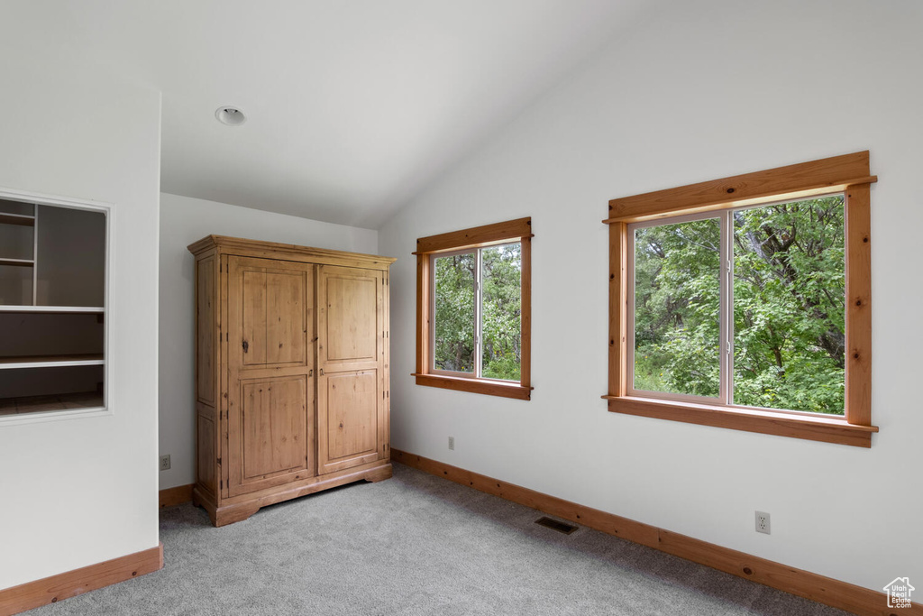 Unfurnished bedroom with high vaulted ceiling, light carpet, and multiple windows