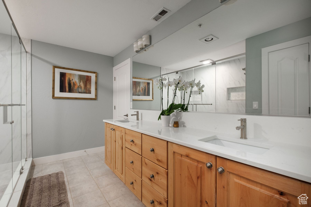 Bathroom featuring tile floors, an enclosed shower, vanity with extensive cabinet space, and dual sinks