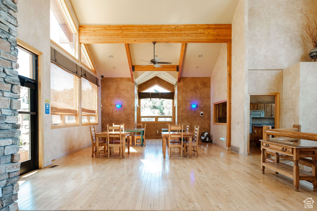 Dining space featuring high vaulted ceiling, beamed ceiling, ceiling fan, and light hardwood / wood-style floors