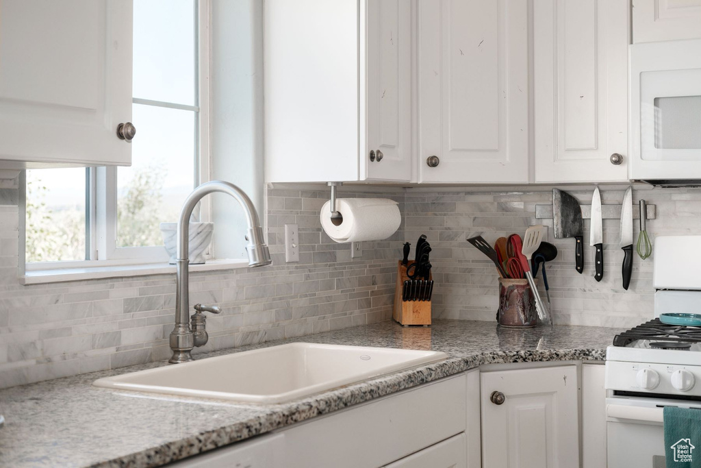 Kitchen with backsplash, white cabinets, sink, and white appliances