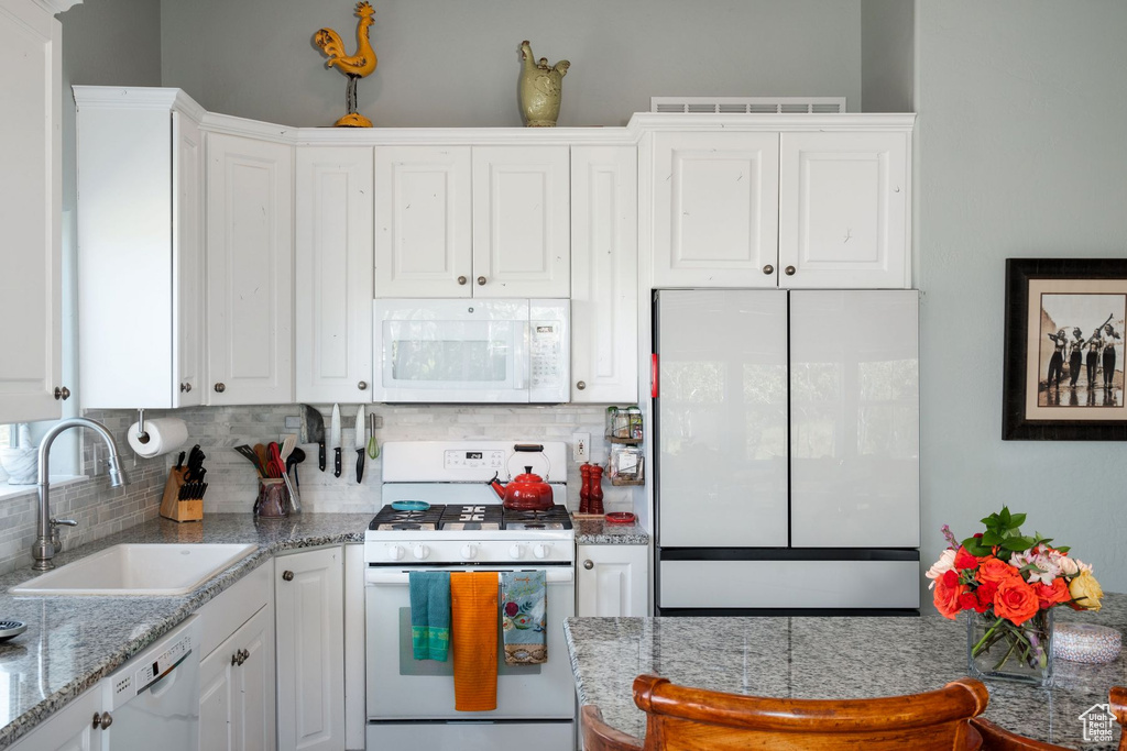 Kitchen featuring sink, white cabinetry, white appliances, and tasteful backsplash